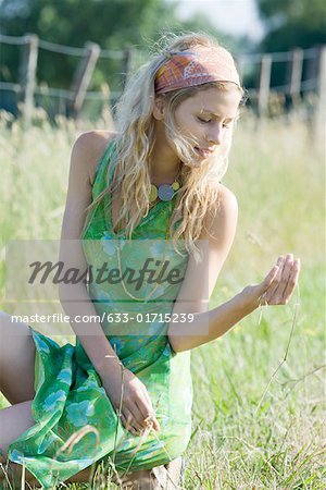 Jeune femme en robe accroupi dans champ, regardant le brin d'herbe