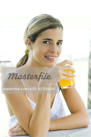 Young woman holding glass of orange juice up to mouth, smiling at camera