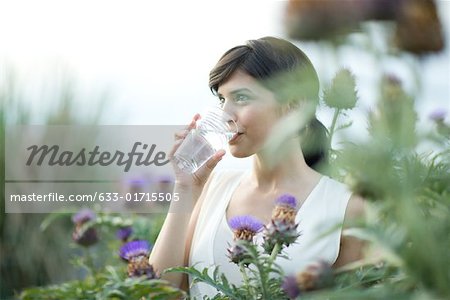Jeune femme à boire d'eau en plein air, entourée de fleurs du chardon-Marie