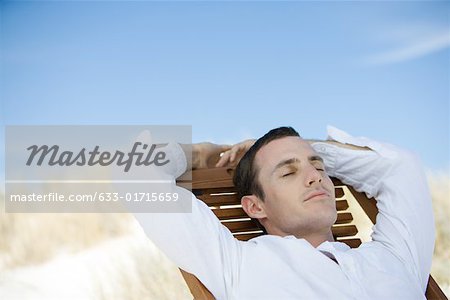 Young man sitting on deckchair, eyes closed