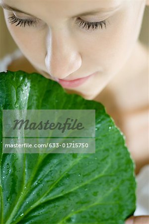 Young woman holding leaf up to face, close-up, cropped