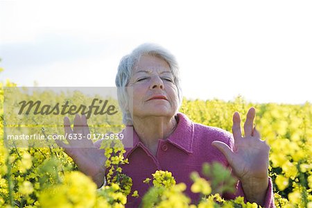 Haute femme debout dans le champ de canola, les yeux fermés, les mains vers le haut