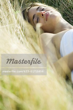 Young woman lying in field with eyes closed, cropped view