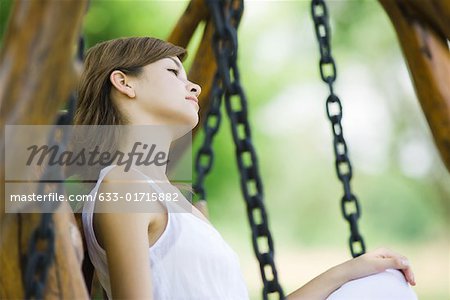 Young woman sitting on swing, looking away, side view