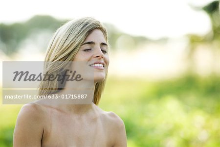 Young woman with bare shoulders, outdoors, eyes closed, smiling