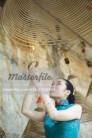 Young woman dressed in traditional Chinese clothing lighting spiral incense hanging from ceiling, low angle view