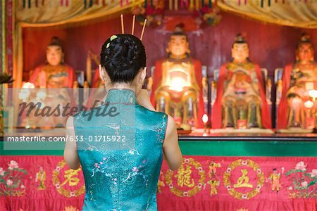Young woman dressed in traditional Chinese clothing standing at shrine, rear view