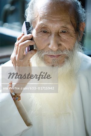 Elderly man in traditional Chinese clothing with long beard, using cell phone