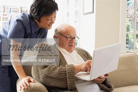 Senior Man à l'aide de l'ordinateur portable avec femme regardant par dessus son épaule
