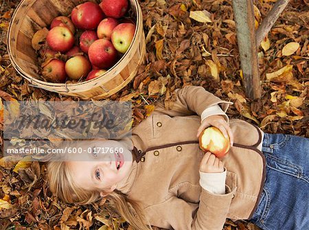 Portrait de jeune fille couchée dans les feuilles de l'automne avec panier de pommes