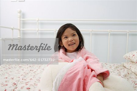 Jeune fille assise sur un lit dans la chambre à coucher, en levant, souriant