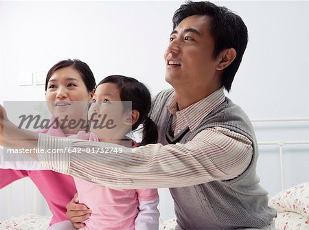 Young couple playing with their daughter in the bedroom, looking away