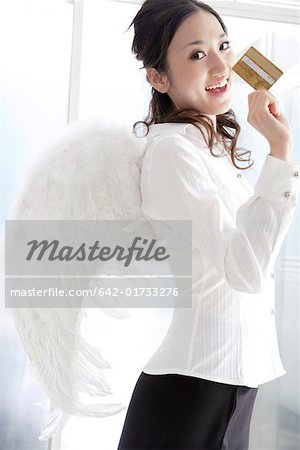 Portrait of a young woman wearing angel wings and holding credit card