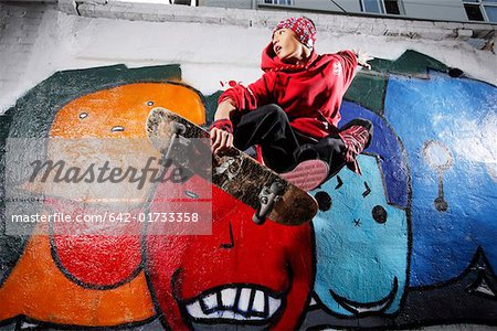 Young man skating board in front of graffiti