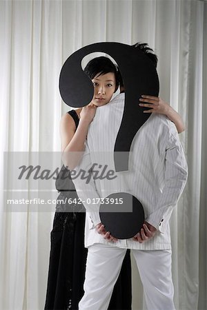 Young woman embracing man and holding question mark sign