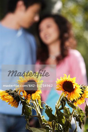 Young couple smiling with sunflower in foreground