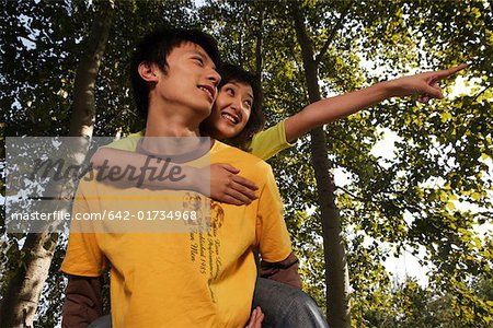 Young man giving woman piggyback ride, smiling, pointing