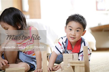 Portrait of a boy with sister building a tower with wooden building blocks