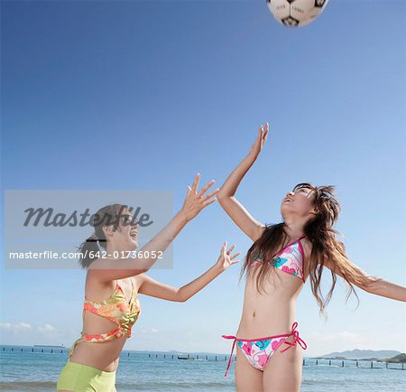 Two young women playing volleyball on beach