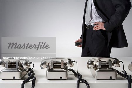 Midsection of a businessman standing by desk with telephones