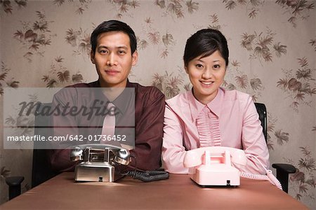 Jeune homme d'affaires et femme assise au bureau avec téléphone, sourire, portrait