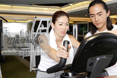 Young man instructing young woman on stair climbing machine