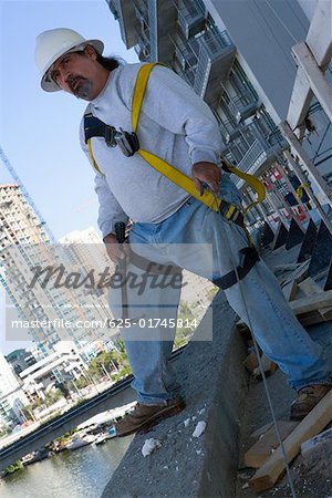 Mature man standing at the edge of a building and holding a hammer