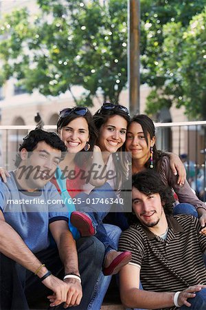 Portrait de trois jeunes femmes et deux jeunes hommes assis ensemble et souriant