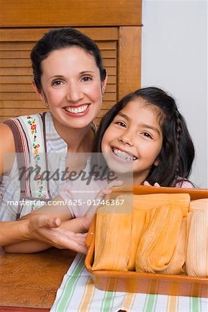 Portrait of a girl and her mother smiling with a tray of breads in the kitchen