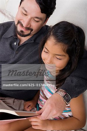 Mid adult man and his daughter reading a book