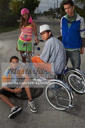 Portrait of a teenage boy on a low rider bicycle with his three friends beside him