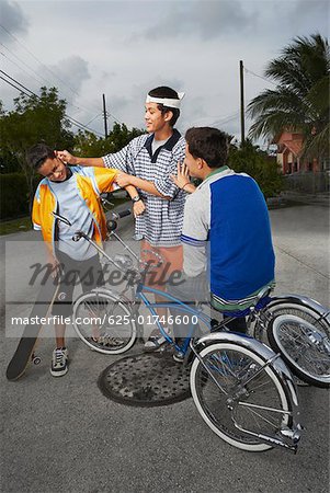 Teenage boy sitting on a low rider bicycle and looking at his friend pulling the ear of a boy