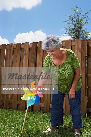 Senior Woman holding ein Windrad in einem Hinterhof und Lächeln