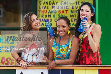 Portrait de trois jeunes femmes accoudée à une balustrade et tenant des bouteilles d'eau