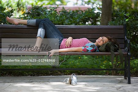Jeune femme à l'écoute d'un lecteur MP3 et couché sur un banc