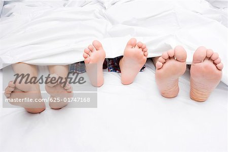 Close-up of a couple's feet with their child on the bed