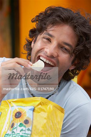 Portrait of a young man eating potato chips