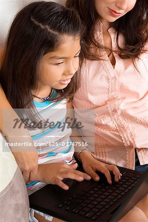 Profil de côté d'une jeune fille assise avec sa mère et à l'aide d'un ordinateur portable