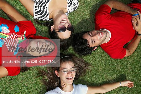 Trois jeunes femmes avec un jeune homme couché sur l'herbe et souriant