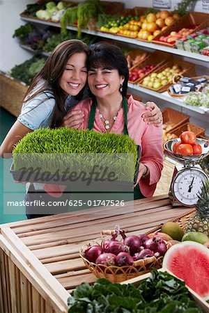 Portrait of a mature woman and her daughter standing with a tray of wheatgrass in a grocery store and smiling