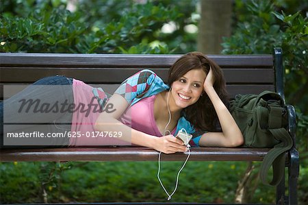 Junge Frau, einen MP3-Player anhören und liegen auf einer Bank