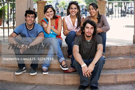 Deux jeunes hommes avec trois jeunes femmes assis sur les marches et souriant