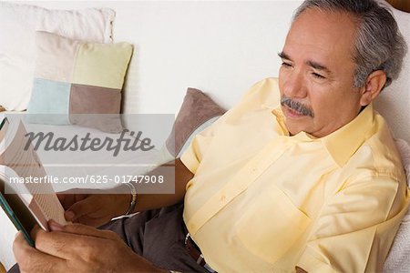 High angle view of a senior man sitting on a couch and holding a book