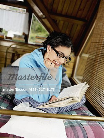 Junge Frau sitzt auf dem Bett und liest ein Buch