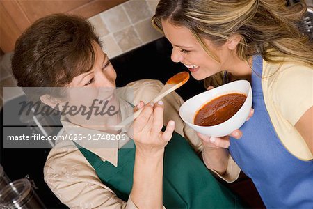 Senior woman feeding tomato soup to her daughter in the kitchen