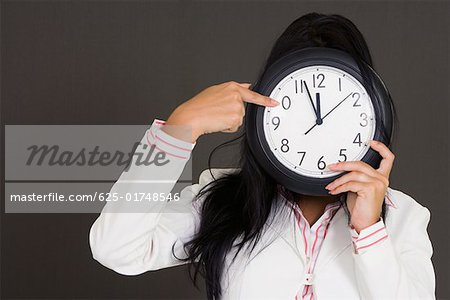 Close-up of a businesswoman holding a clock in front of her face and pointing