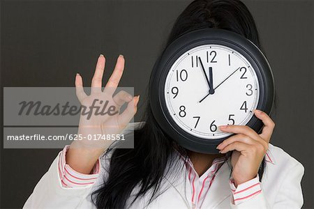 Close-up of a businesswoman holding a clock in front of her face and making an OK sign