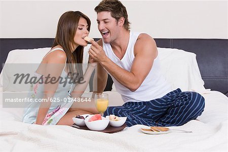 Mitte erwachsener Mann Fütterung Frühstück mit einer jungen Frau auf dem Bett
