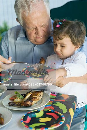 Senior man feeding his granddaughter with a fork