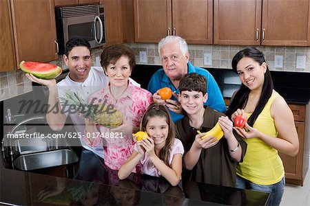 Portrait d'une famille de trois générations tenant des fruits dans la cuisine